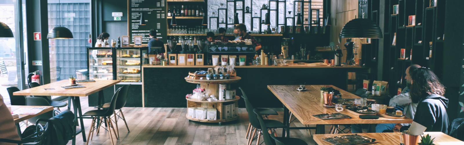 a cafe with tables and chairs in the foreground, a coffee bar in the background